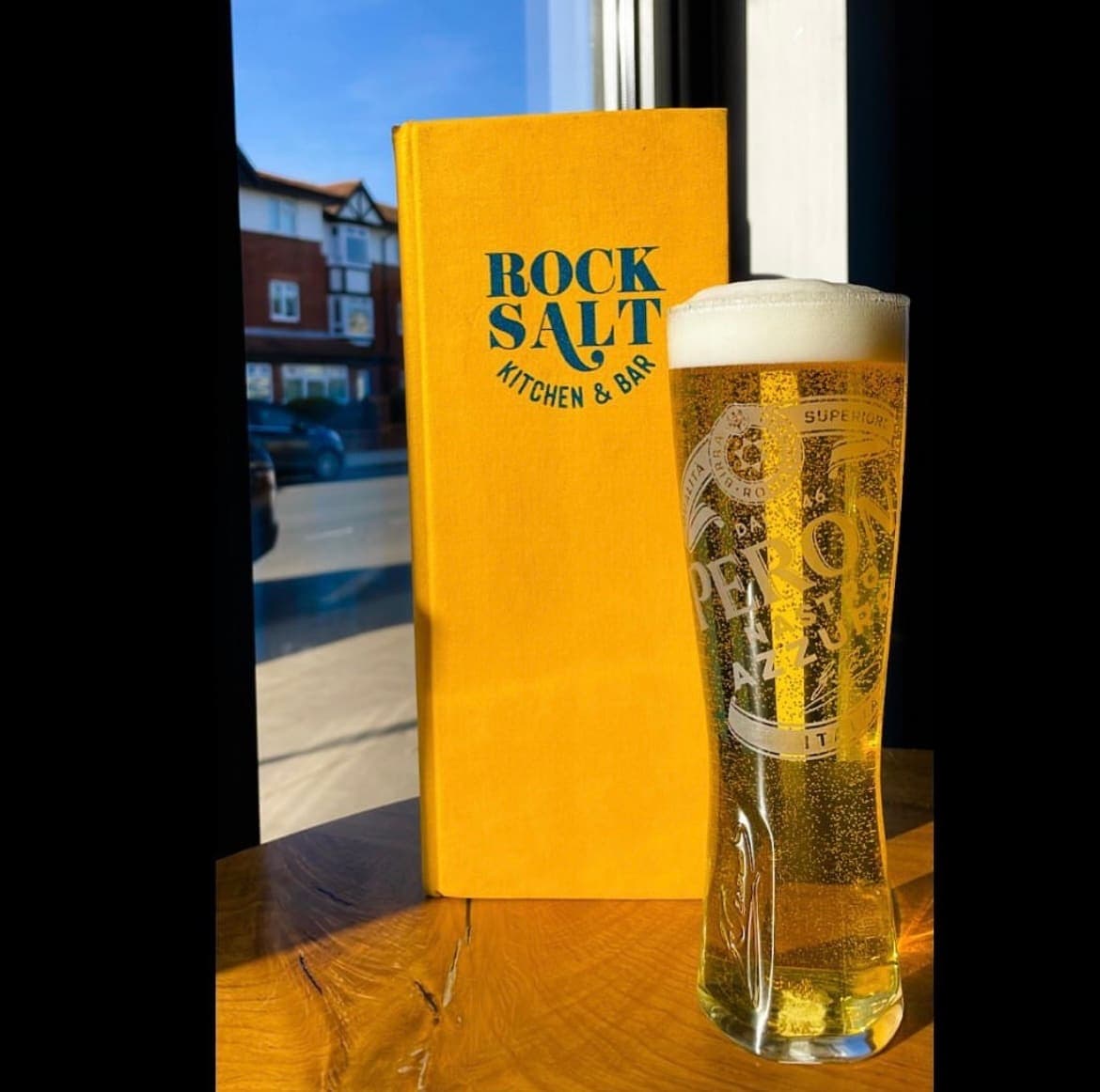 A cold glass of lager on the bar in front of the window