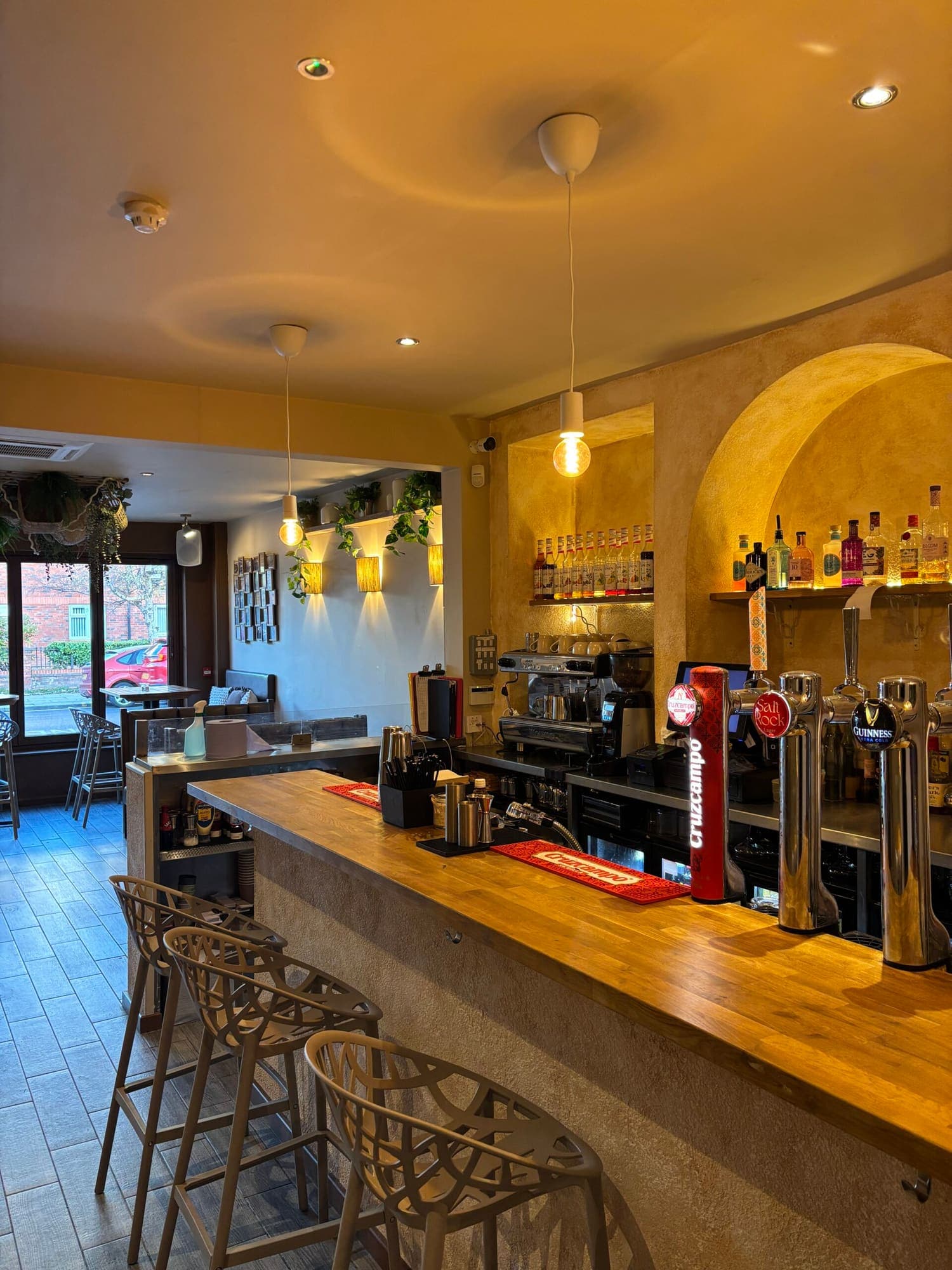 The long wooden bar with beer taps and coffee machine, daylight coming in from the street windows