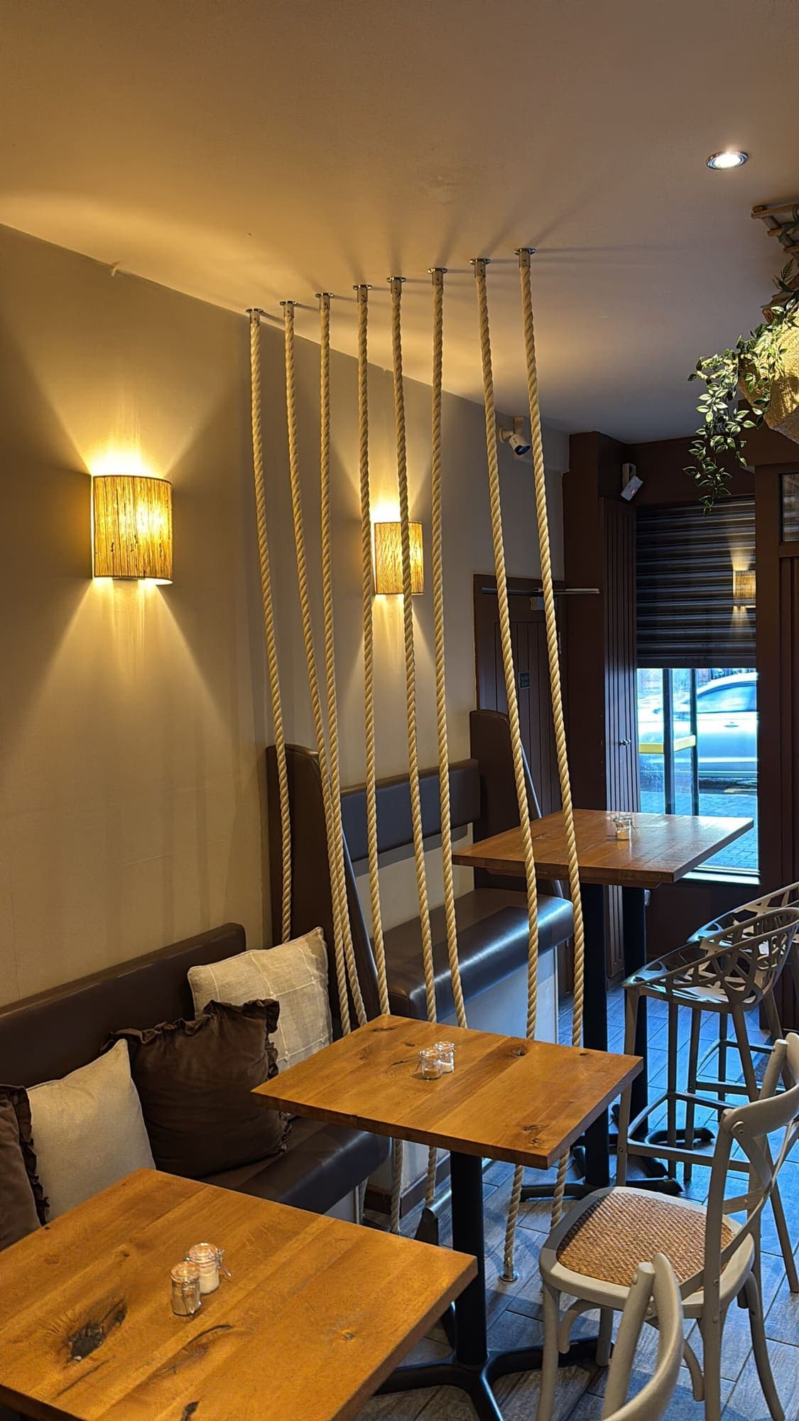 Rope swing seats at a window table, lit by textured wall lamps