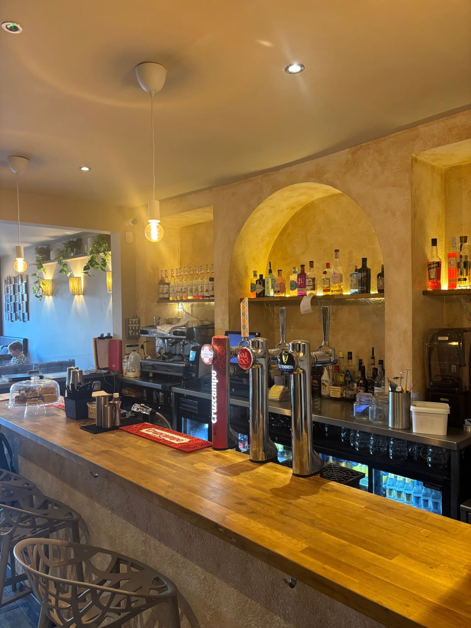 The bar at Salt Rock, with spirits lit in an arched alcove and wall lamps along the plastered wall