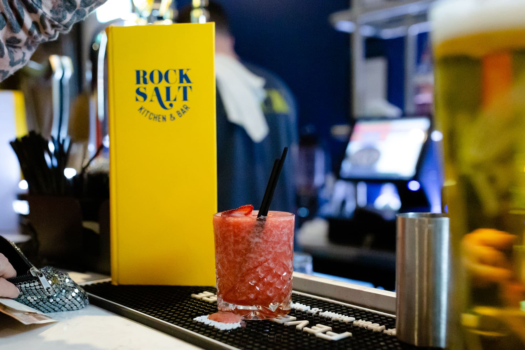 A tall red cocktail garnished and served over ice on the bar top