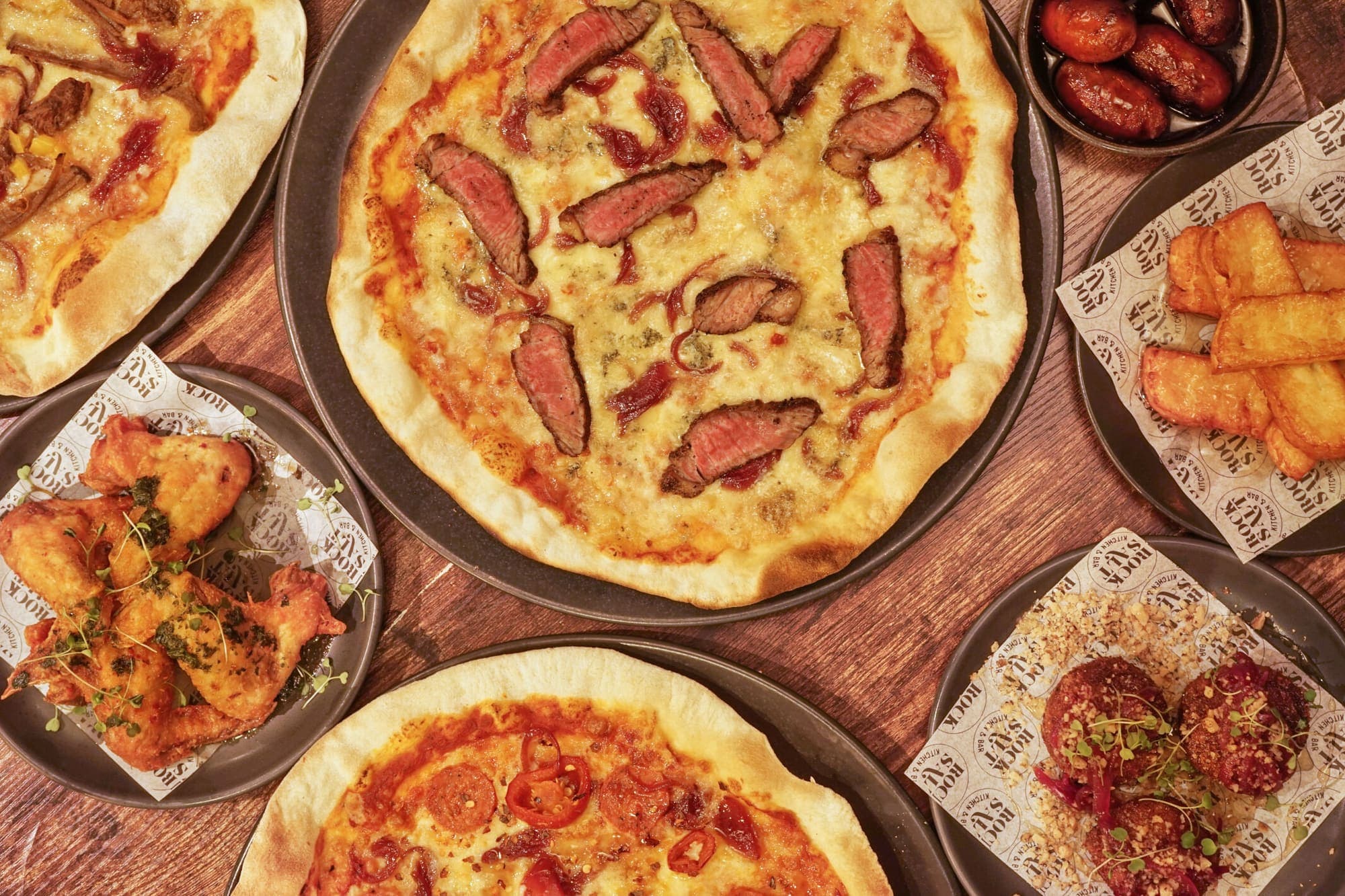 Three thin-based pizzettas on wooden boards, one topped with sliced sausage